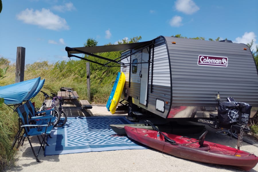Perfect RV rental setup! Travel trailer with awning, kayaks, bikes, and picnic area for a relaxing outdoor camp.
