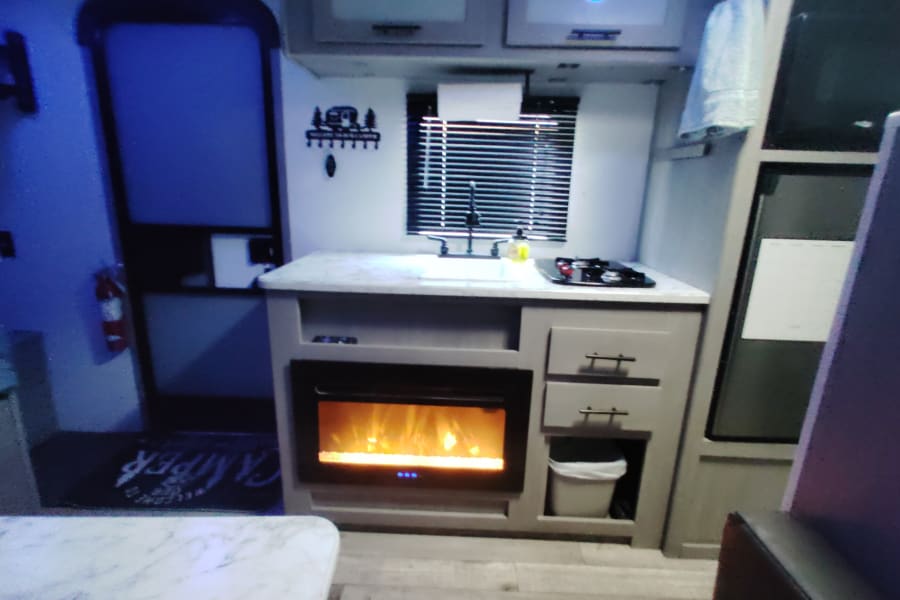 Inside an RV rental: a cozy kitchen with sink, stove, and electric fireplace. Perfect compact living for road trips.