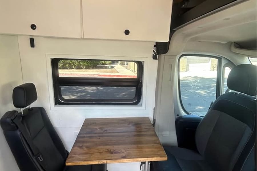 RV rental interior: wooden ceiling, overhead storage, dining table, two seats, and a window. Ideal for campervan adventures.