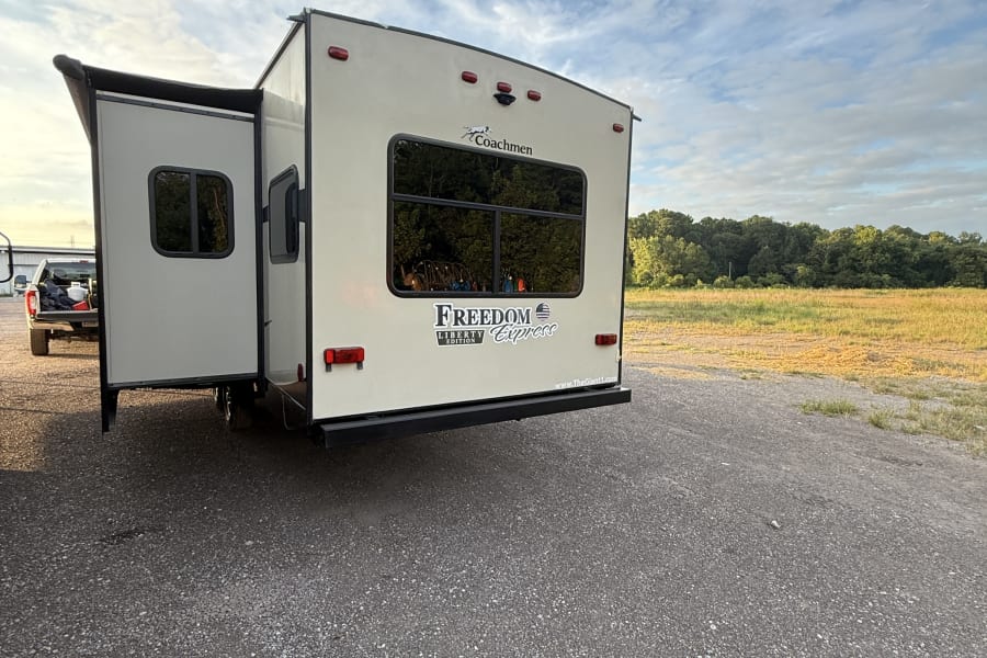 This **Coachmen Freedom Express travel trailer**, an ideal **RV rental**, is set up on a gravel lot, ready for outdoor adventures.