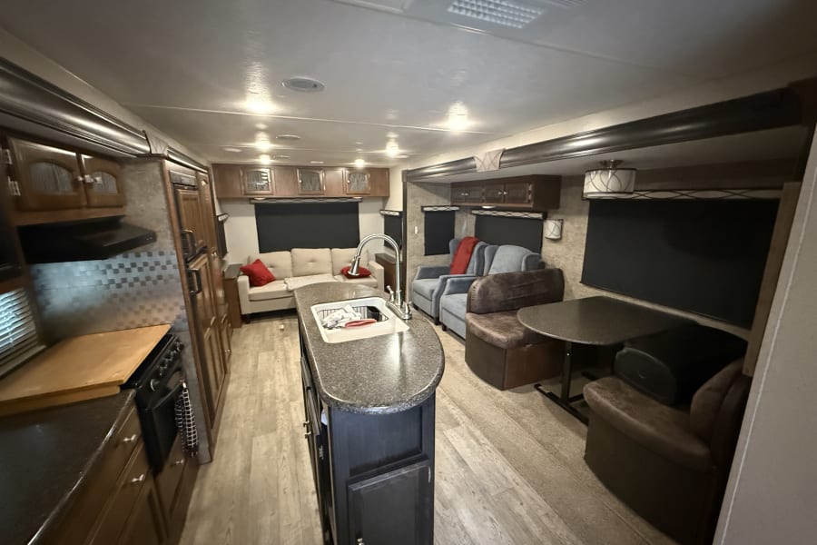 Spacious RV rental interior showcasing a full kitchen with island, living room with sofa, and dining booth.