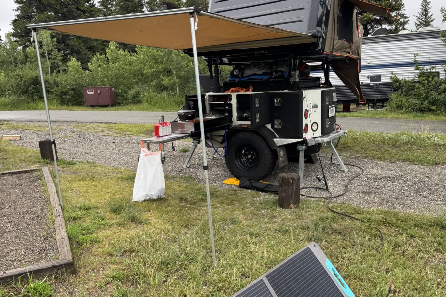 RV rental campsite setup: overland camper, awning, and portable solar panel for comfortable outdoor travel.