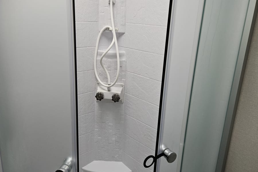 This RV rental features a compact, white shower with a handheld showerhead and frosted doors.