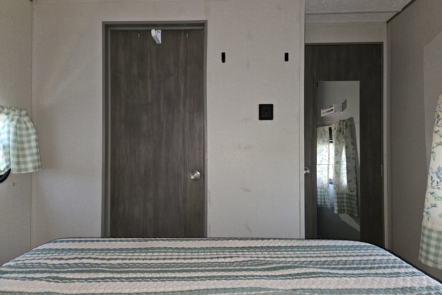 Compact RV rental bedroom featuring a striped bed, two doors, and patterned curtains. Cozy travel space.