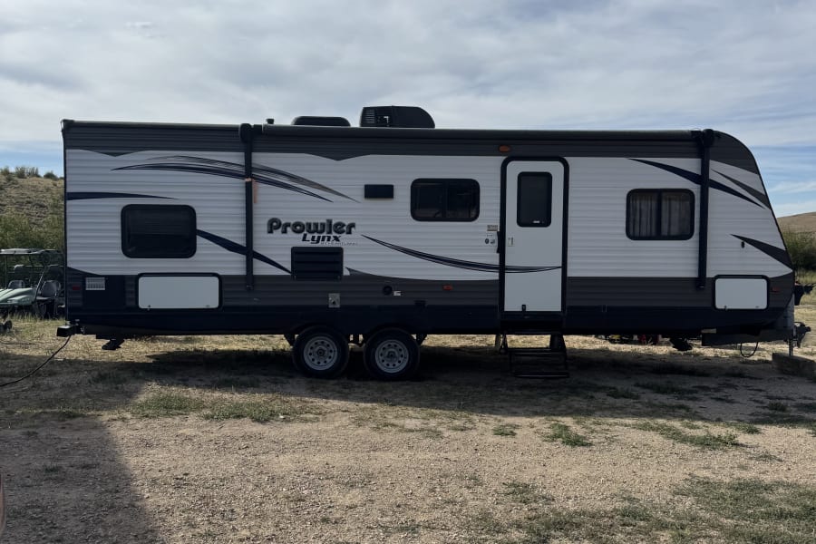 Prowler Lynx travel trailer, an RV rental, on a gravel lot under a cloudy sky, ready for camping.