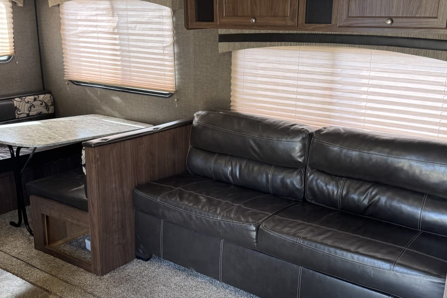 Inside an RV rental, a well-appointed living space with a black leather sofa, dining booth, and wood cabinets.