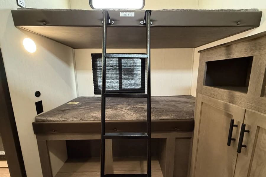 RV rental interior featuring bunk beds with a ladder. The top bunk has a 300 lb capacity, providing a compact sleeping area.