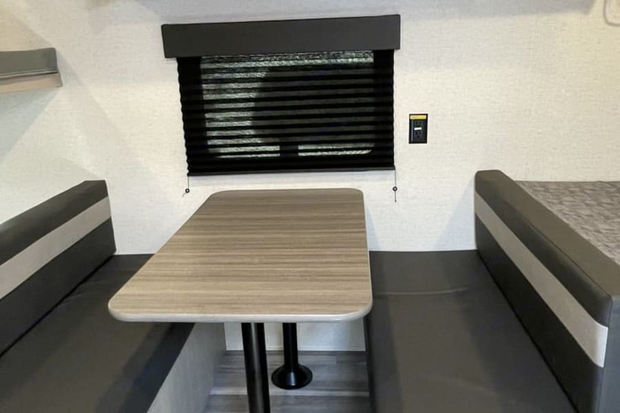 This RV rental features a cozy dinette with a table and benches, and a glimpse of a bed, ready for adventures.