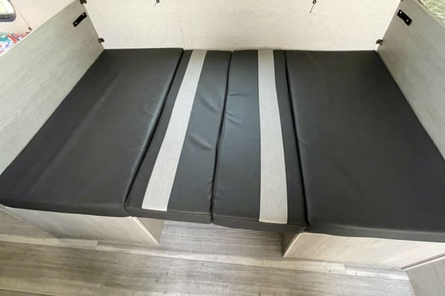 A cozy RV rental bed setup: dark gray cushions on light wood storage bases, ideal for sleeping.