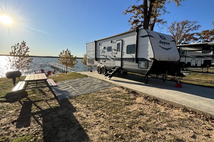 Peaceful lakefront rv rental with a travel trailer parked under a sunny sky by a dock, ready for camping.