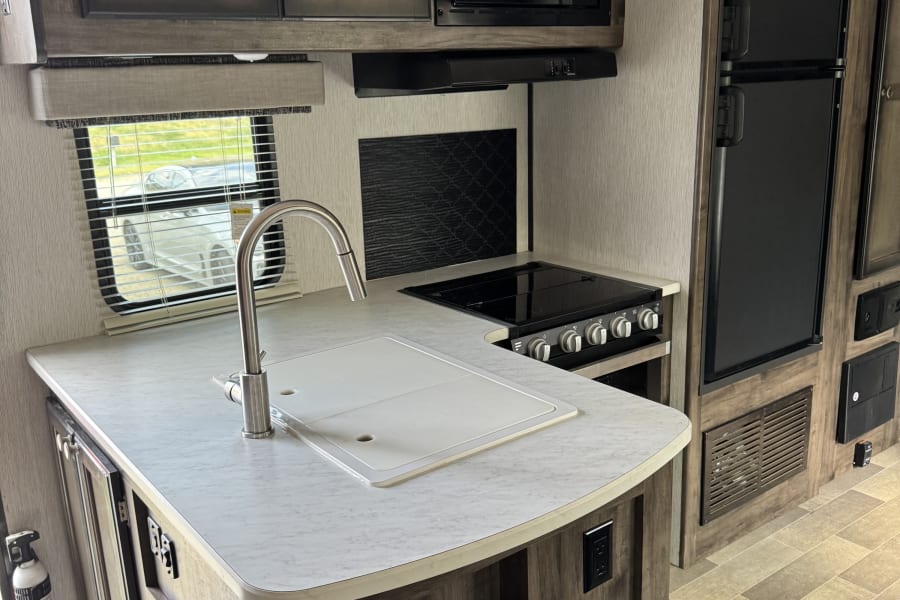 RV rental kitchen interior: white countertop, sink, black stove, microwave, and refrigerator, plus ample storage.
