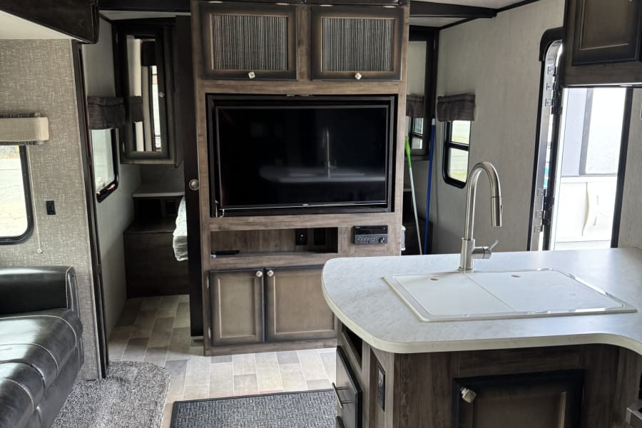 RV rental interior showing a modern kitchen with sink, entertainment center, and sofa in a well-lit space.