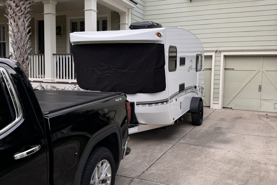 Preparing for an outdoor adventure: a black pickup truck hitched to a compact RV rental in a driveway.