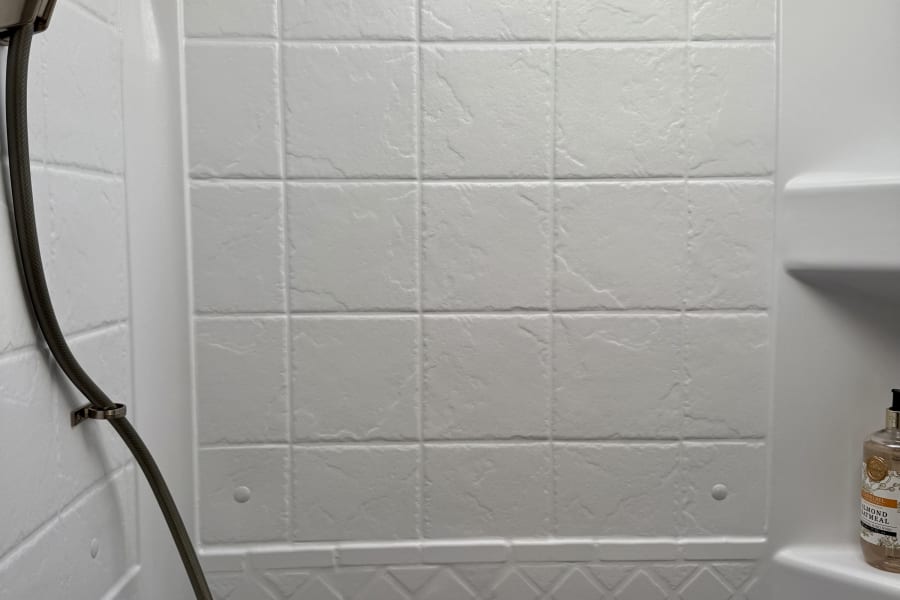 Clean and compact RV rental shower interior, featuring a handheld showerhead, textured walls, and built-in soap shelf.