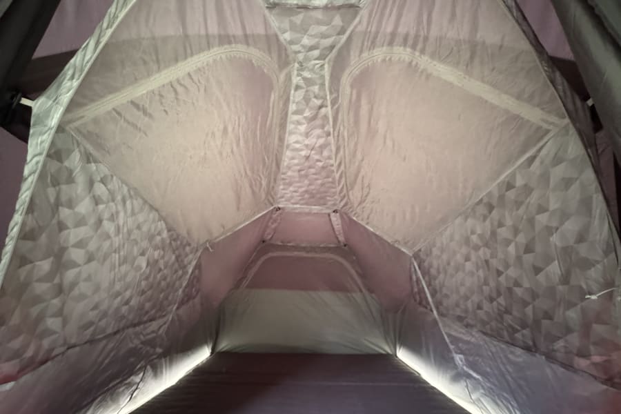 Cozy RV rental pop-up tent interior featuring patterned fabric walls, a plush mattress, and ambient LED lighting.