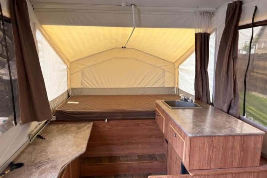RV rental: Inside a pop-up camper, with a bed, a kitchen sink on a speckled counter, and wood-toned floors.