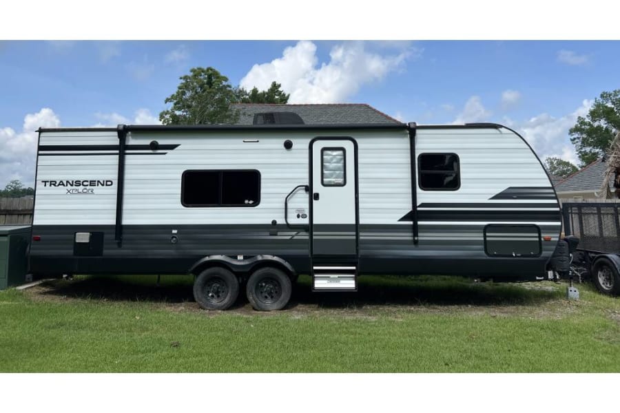 Modern Transcend XPLOR travel trailer for your next adventure. This white and gray RV rental is parked on grass under a blue sky.