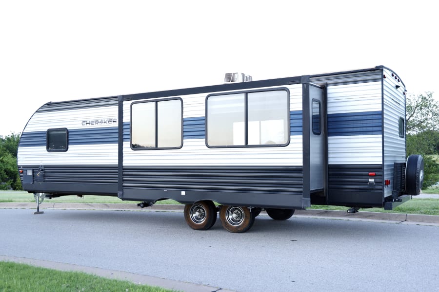 Side view of a white & blue Cherokee travel trailer RV rental, with an extended slide-out. Ready for your next camping adventure!