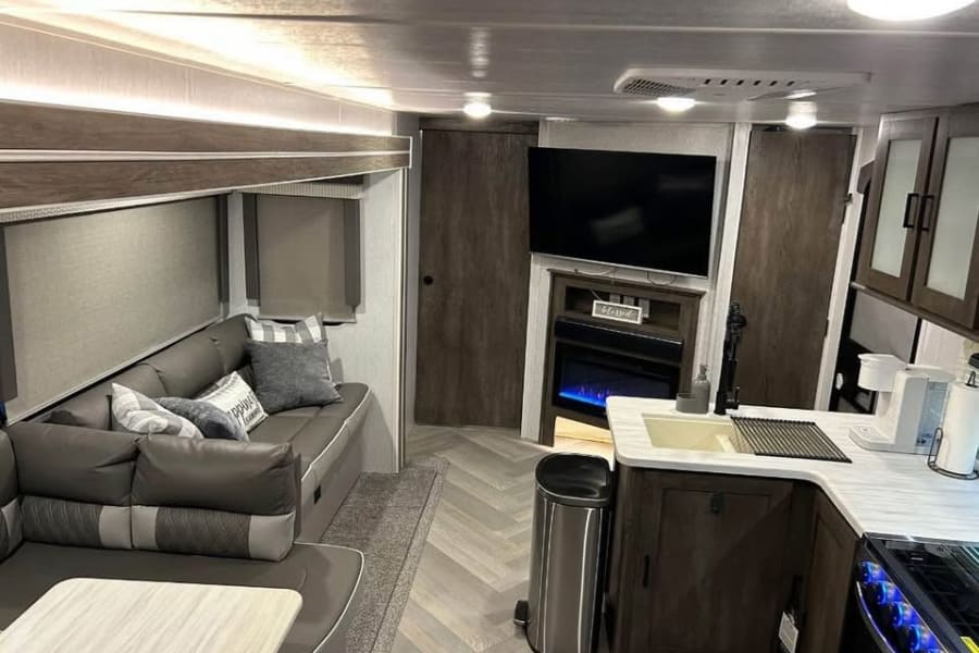 Spacious RV rental interior: modern living area with sofa, TV, fireplace, and functional kitchen.