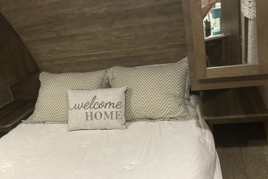 This RV rental bedroom offers a comfortable bed, overhead storage, and a mirrored cabinet door for convenience.