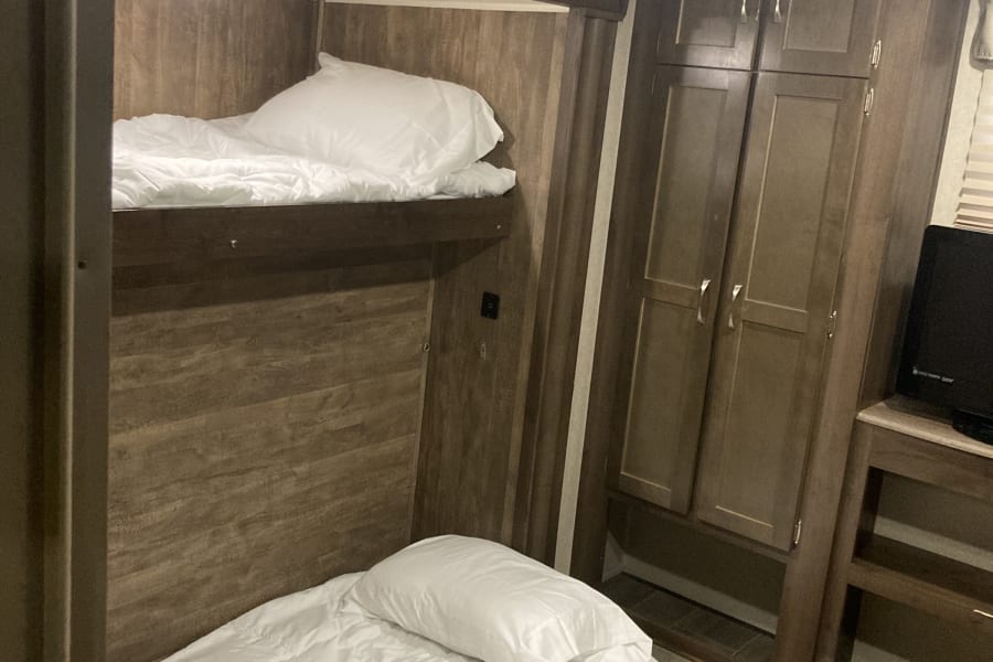Cozy RV rental interior featuring two bunk beds with white bedding, built-in wooden cabinets, and a tiled floor.