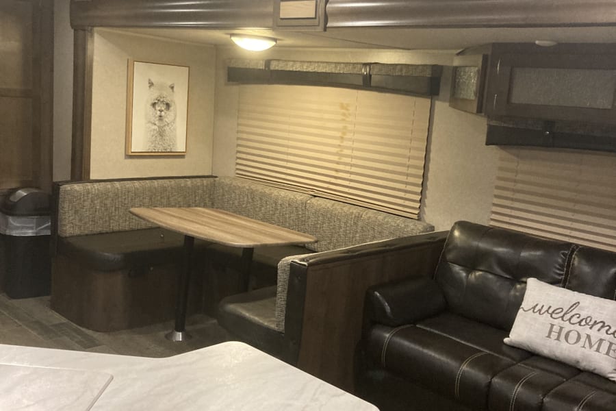 This modern RV rental interior features a booth dinette, comfortable leather sofa, and kitchen counter, defining a cozy living space.