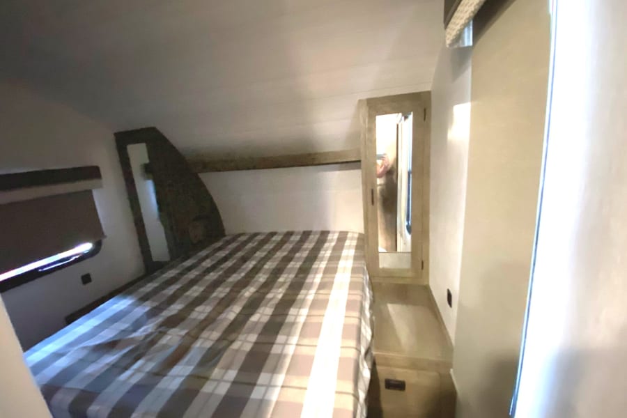 Cozy RV rental bedroom with a plaid bed, window, and mirrored cabinet. Perfect for your next adventure.