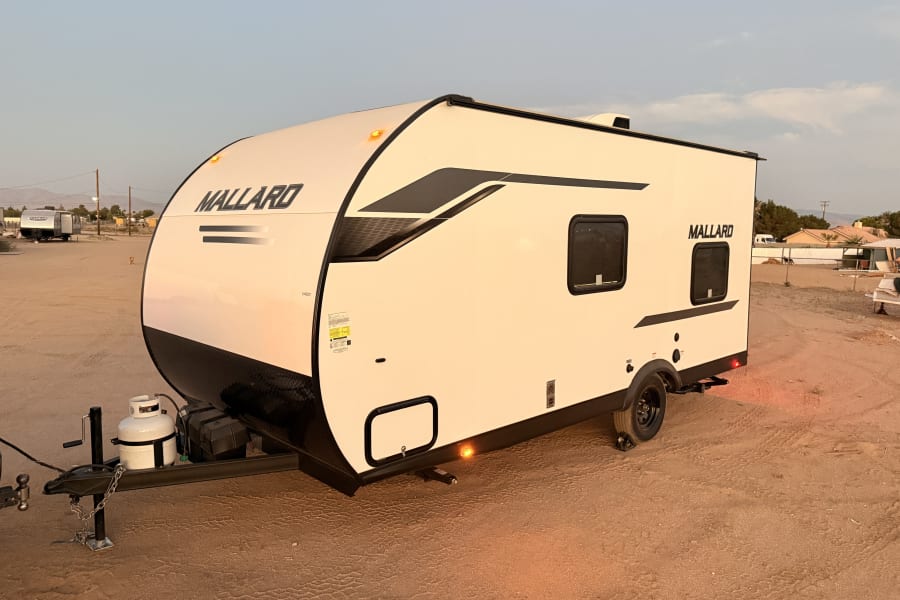 White & black Mallard travel trailer, ready for your RV rental journey, parked on a sandy lot.