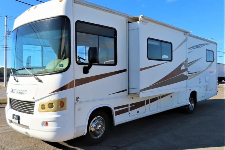 A white Georgetown RV rental with its slide-out extended, parked on asphalt under a blue sky, ideal for travel.