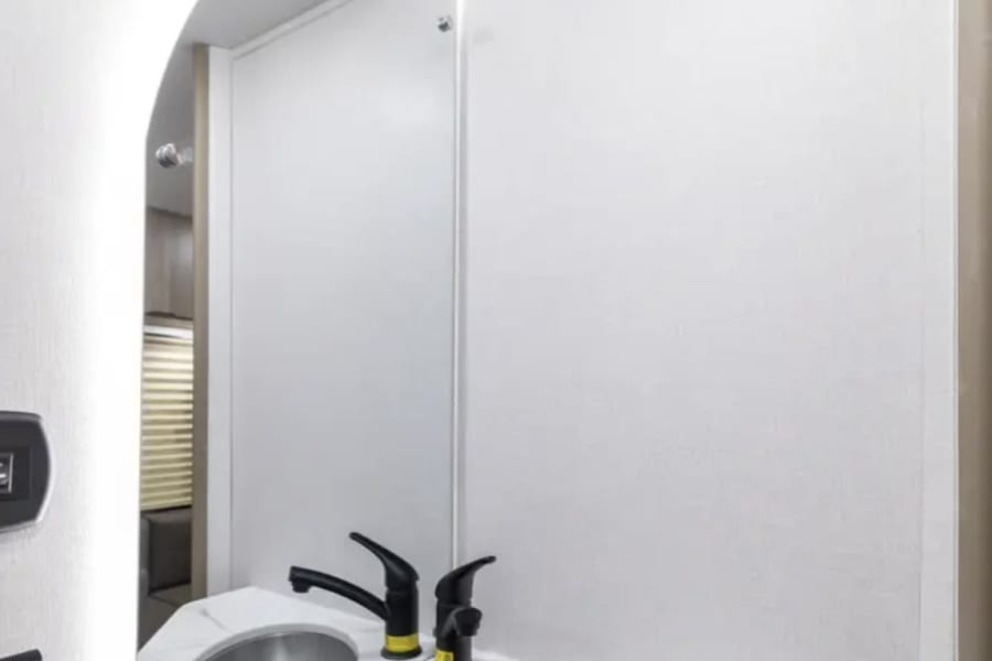 This RV rental's modern vanity boasts a corner sink, stylish black faucets, and an arched, illuminated mirror.