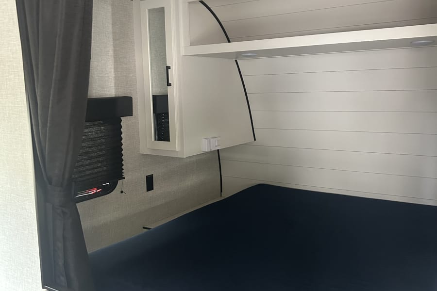 Compact RV rental bedroom featuring a dark blue bed, white shiplap wall, and privacy curtain. Ideal for mobile living.