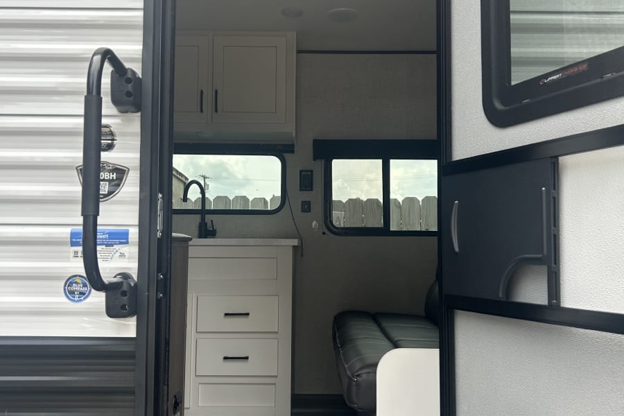 Modern RV rental interior: A compact kitchen with sink & cabinetry, and a cozy seating area. Ideal for travel.