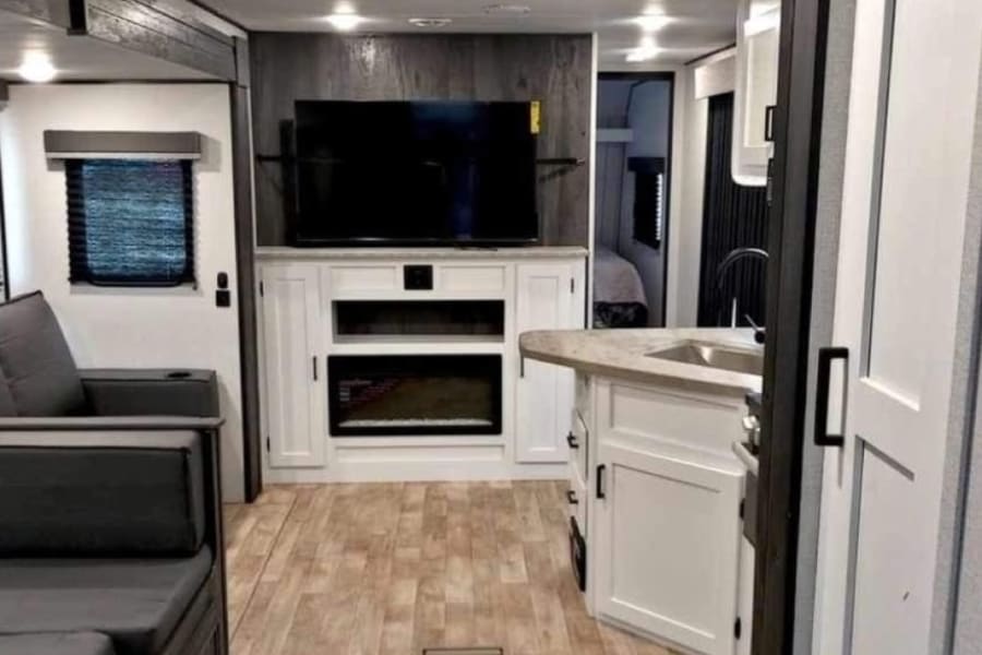 Spacious RV rental interior: modern living area with sofa, kitchen island, and entertainment center with fireplace.