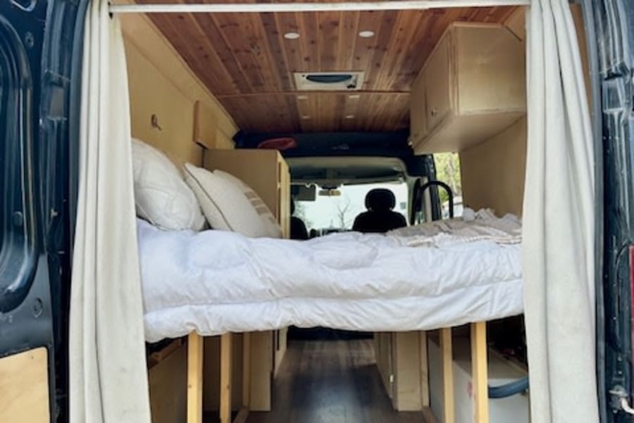 Explore this RV rental's custom camper van interior featuring an elevated bed, wood accents, and ample storage space.
