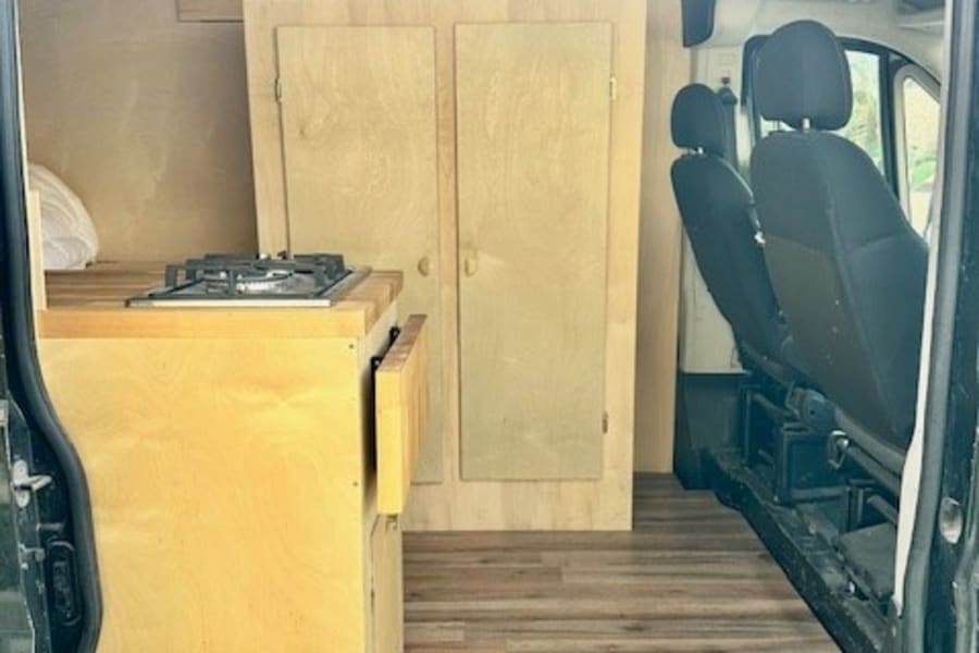 Spacious van conversion interior, ideal for rv rental adventures. Features wood paneling, kitchen unit, & cozy rug.
