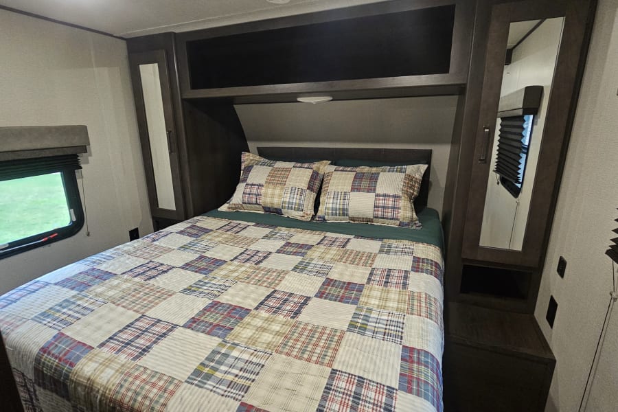 Experience comfort in this cozy RV rental bedroom. Features a patchwork bedspread, ample storage, and a scenic window view.