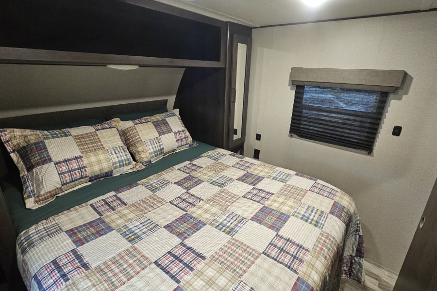 Cozy RV rental bedroom with patchwork bedding, overhead storage, and window. Perfect for your next trip!