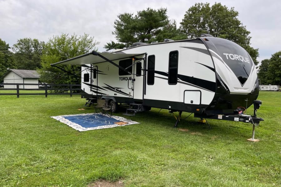 This TORQUE RV rental, a sleek travel trailer, is set up for outdoor camping on a grassy site.