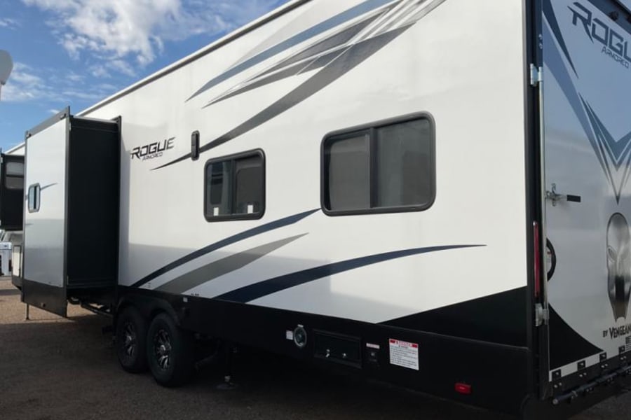 This white "ROGUE ARMORED" toy hauler RV rental, with an extended slide-out and rear ramp, is ready for adventurous travel.