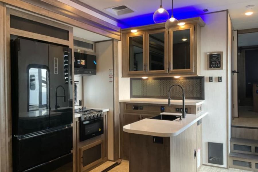 Modern RV rental kitchen interior featuring a large fridge, stove, sink, island, and stylish blue lighting.