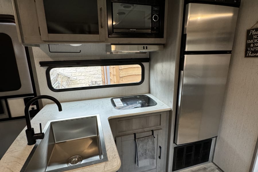RV rental kitchen view: features a modern sink, microwave, refrigerator, and light wood-look flooring.