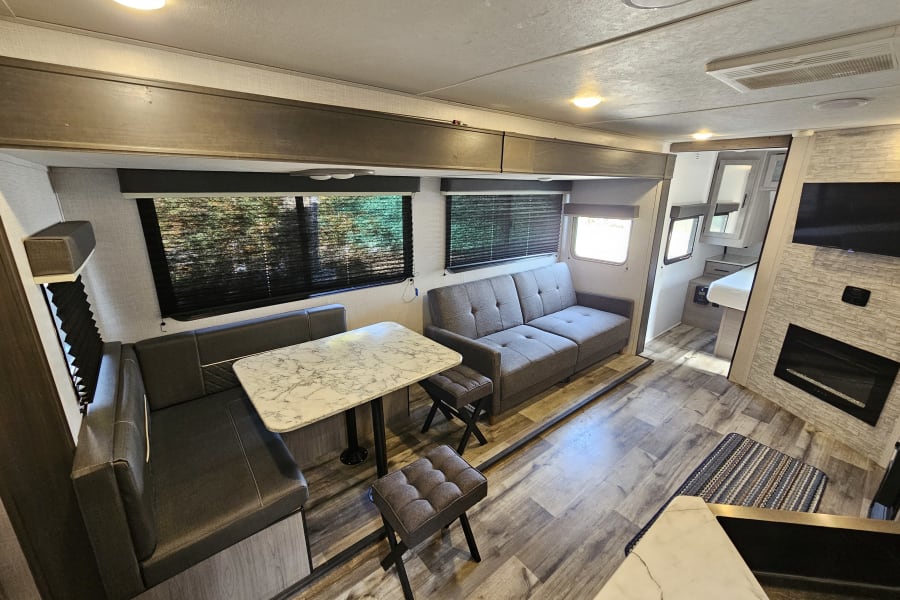 Modern RV rental living area featuring a comfy sofa, dinette, and entertainment center with fireplace.