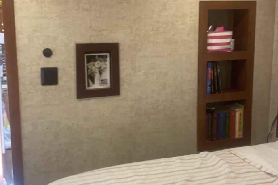Cozy RV rental bedroom with striped bedding, built-in bookshelf, framed picture, and ceiling AC vent.