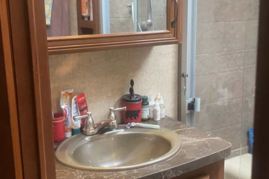 Inside an RV rental bathroom: features a compact vanity with sink, mirror, toiletries, and a glass-enclosed shower.