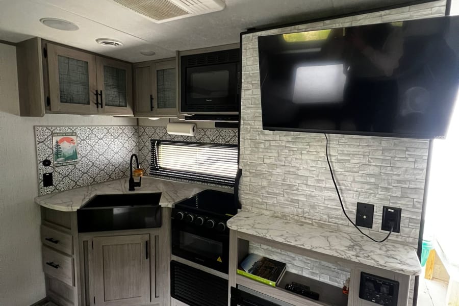 Modern RV rental interior featuring a functional kitchen, entertainment area with TV & fireplace, and wood-look flooring.