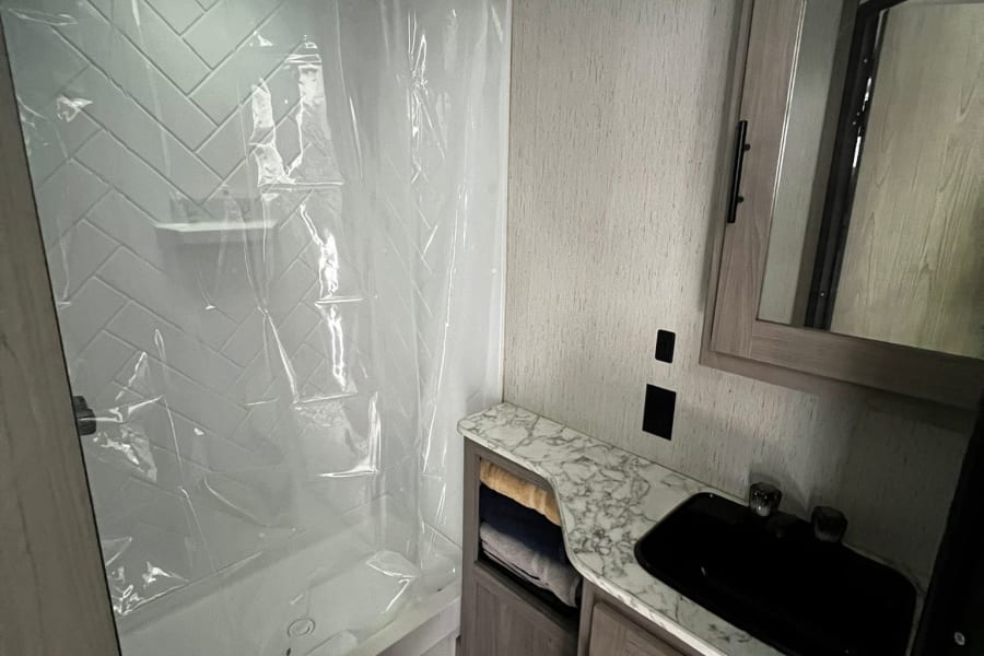 Inside an RV rental: a bright, compact bathroom featuring a shower, toilet, and vanity with black sink.