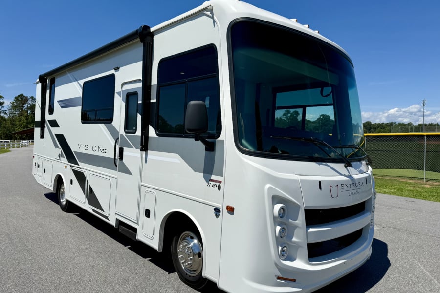 A pristine white Entegra Coach Vision SE 27 ASE RV rental, a modern motorhome, parked on asphalt under a clear blue sky.