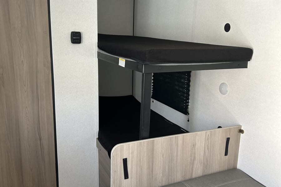 This RV rental shows a clean interior with bunk beds, a wood-look wardrobe, and gray dinette seating. Perfect for your travels.