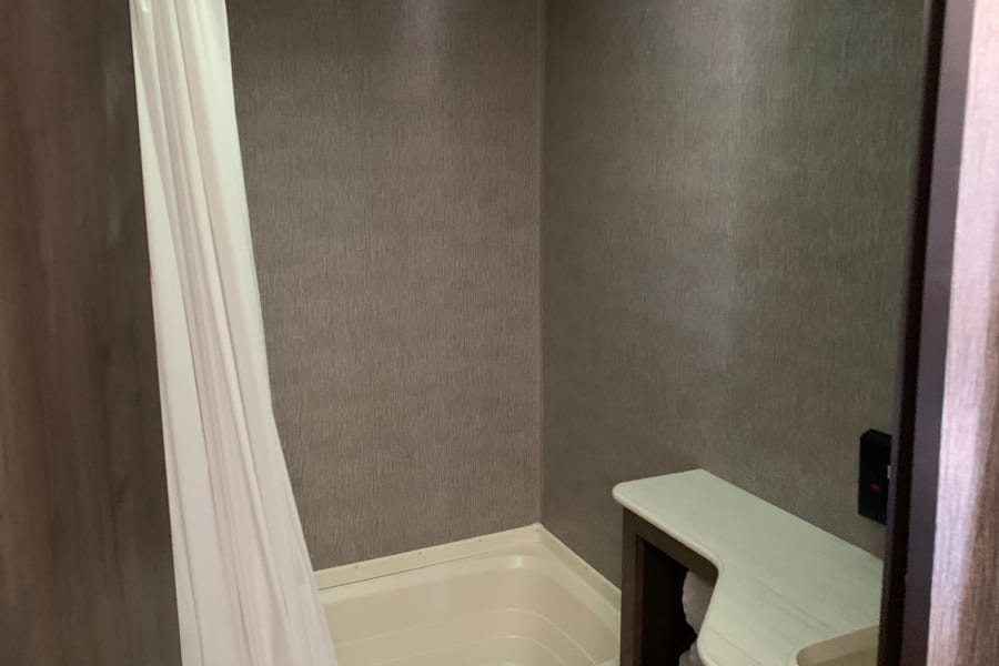 Compact RV rental bathroom with tub/shower, white curtain, toilet, and vanity sink.