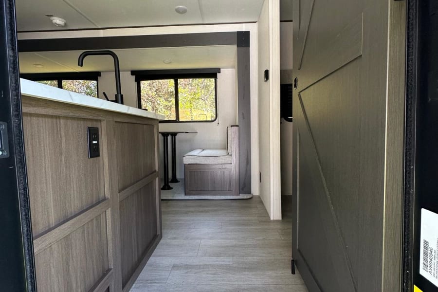 Modern RV rental interior: kitchen island, dining booth, and chic barn door create a cozy living space.